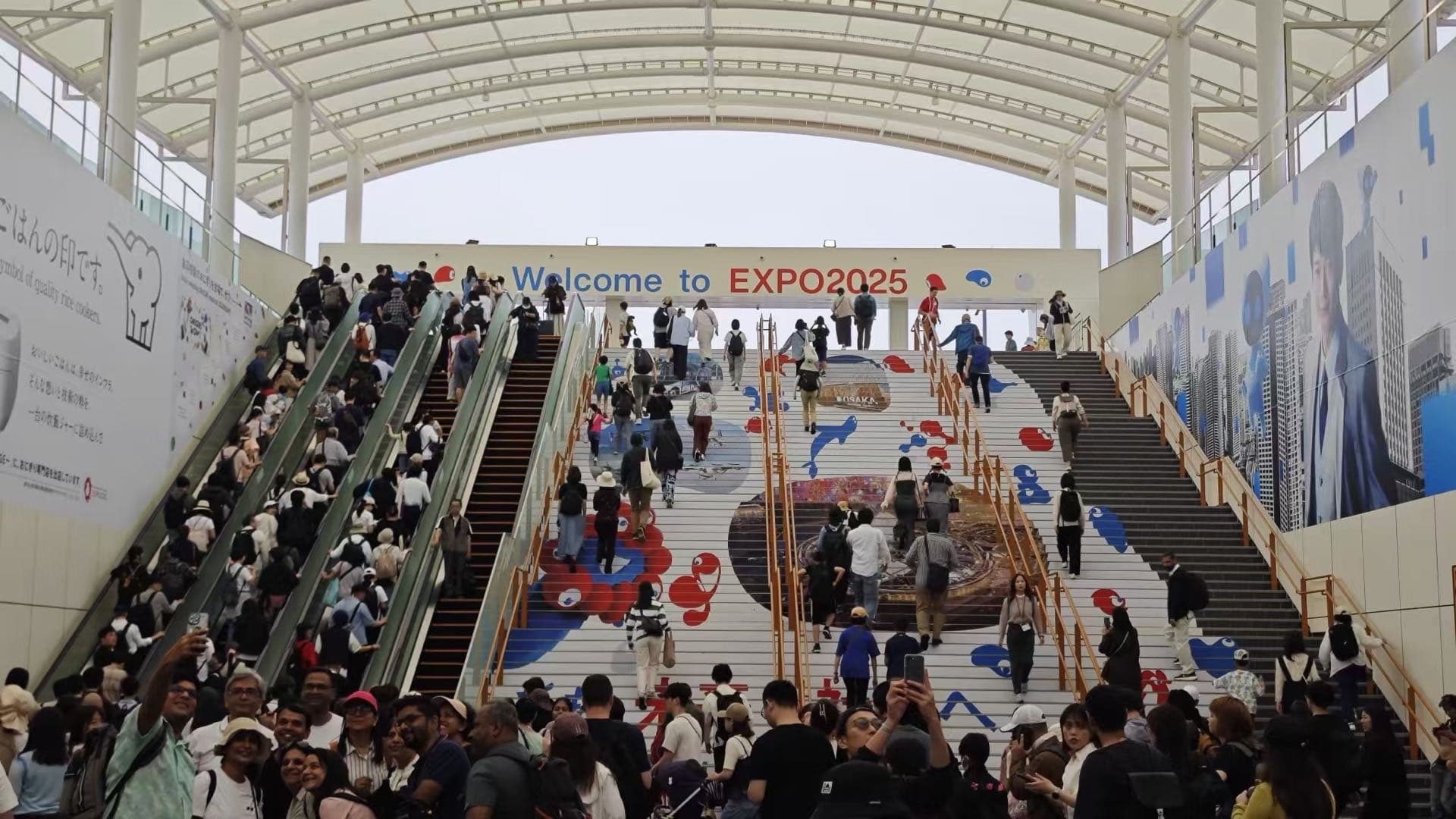 大阪世博会入口通道内有大量游客和 Welcome to EXPO 2025 标语