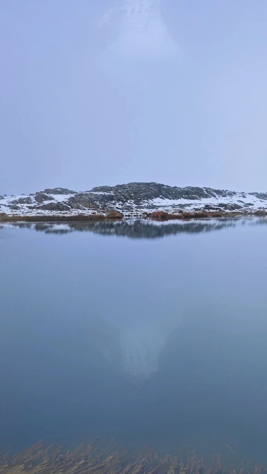 高山湖面映出雪坡和低云，水面平静