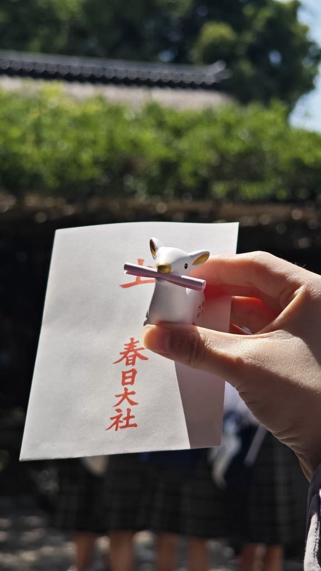 手拿写有春日大社字样的签纸，旁边是鹿形装饰