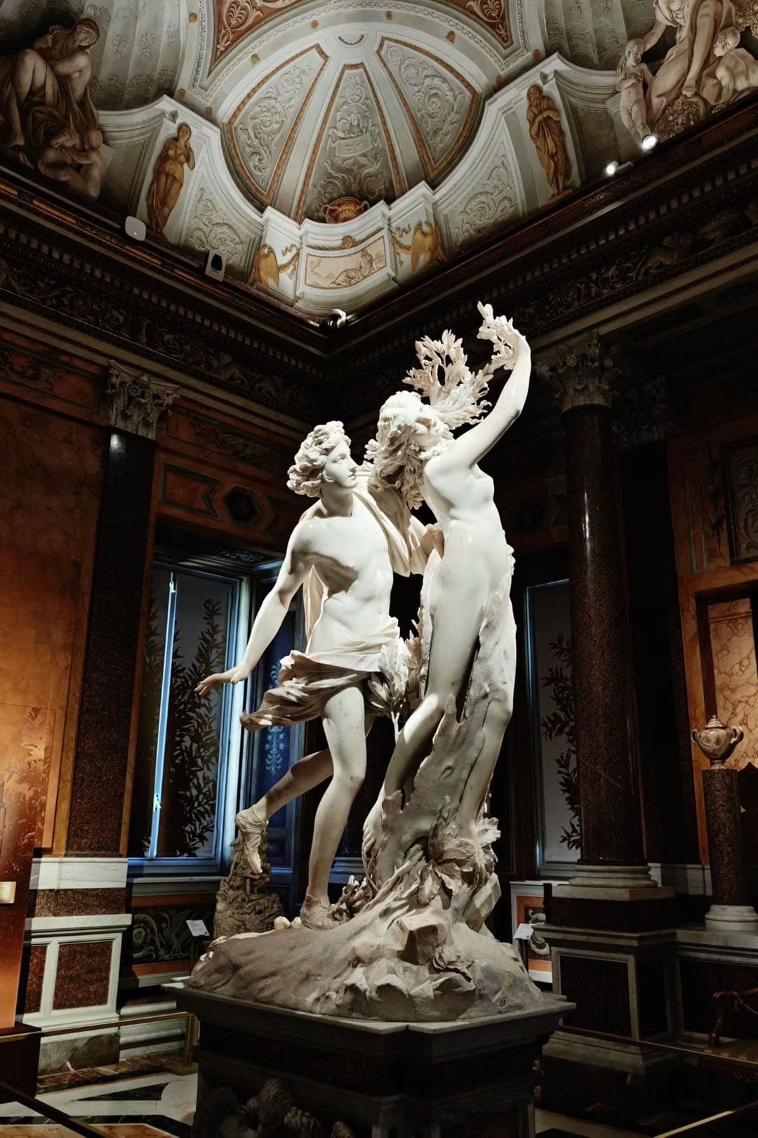 贝尼尼《阿波罗与达芙妮》立在博尔盖塞美术馆展厅中央,背景可见穹顶壁画和深色墙面